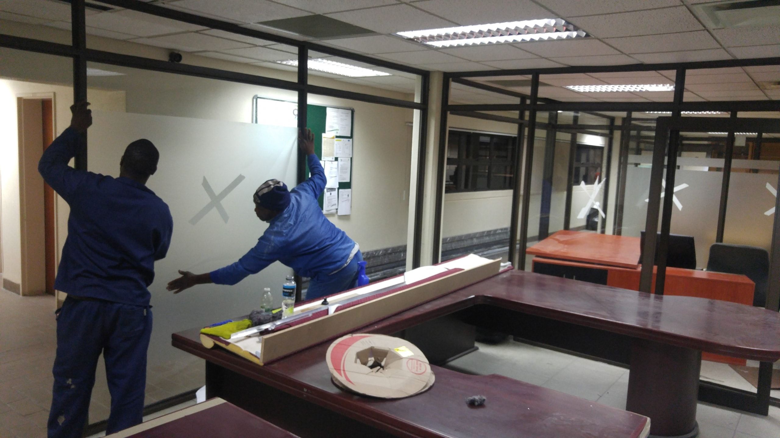 Two installers fitting an aluminium-framed glass partition in an office