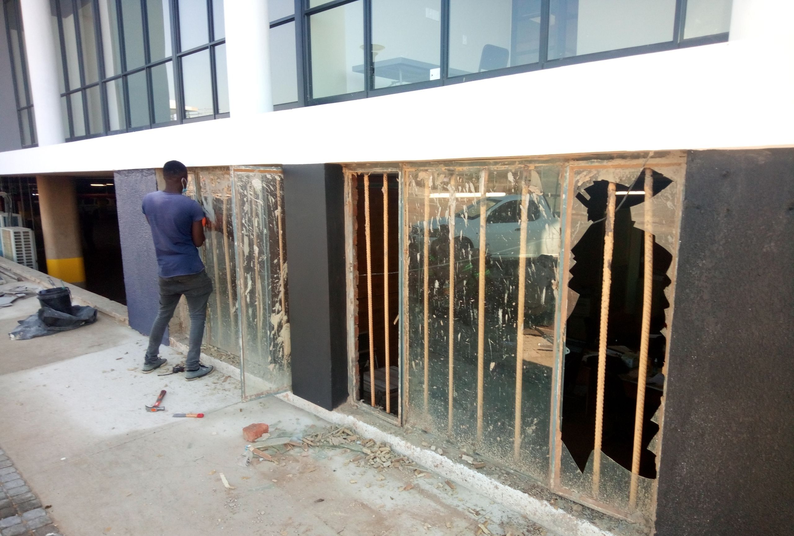 Commercial window with smashed glass panes and a worker clearing the frame