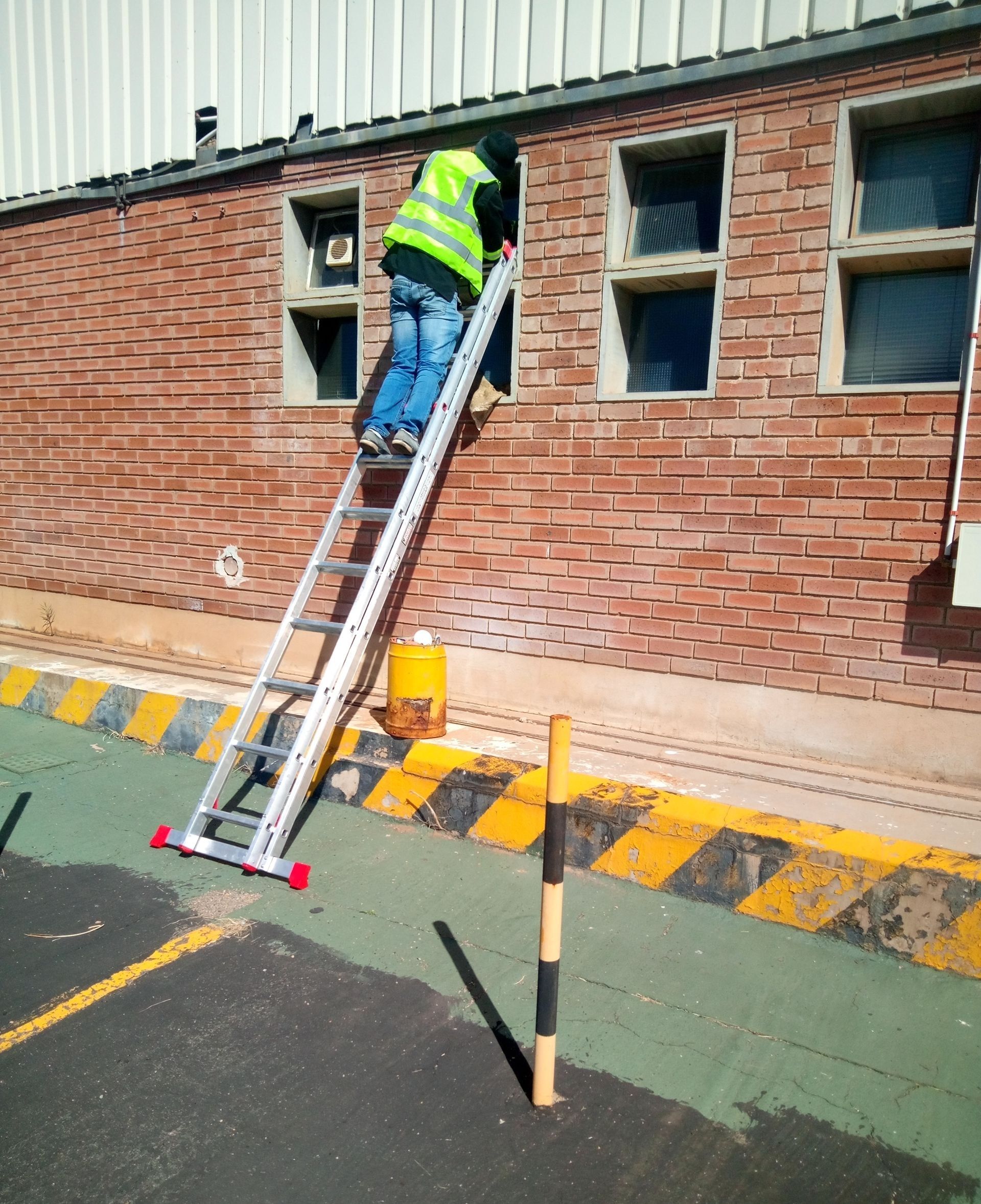 Glazier on a ladder replacing glass in small windows on a brick commercial building